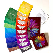 Az Érzésvirág érzelemkártya-készlet teljes tartalma kiterítve: 20 színkategóriára bontott, különböző fő érzelmeket és hozzájuk tartozó altérzéseket összegyűjtő lapok. A kártyák szivárványszerű átmenetben helyezkednek el a képen, a háttérben a módszertani füzet és a díszdoboz is látható. A vizuális elrendezés kiemeli a termék gazdag eszköztárát és terápiás használhatóságát.