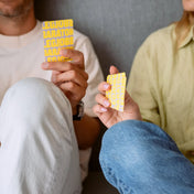 Két ember ül egymás mellett, kezükben tartják a sárga hátlapú „Legjobb barátok” kártyákat. A jelenet bensőséges, baráti pillanatot ábrázol, a játék központi eleme a beszélgetés és a kapcsolódás.