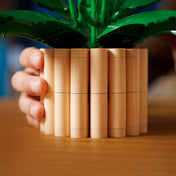 LEGO Botanicals Peace Lily (11504) készlet kaspójának közeli részlete, világosbarna LEGO elemekből épített hengeres virágtartó, amelyet kézben tartanak az asztalon.