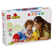 LEGO Duplo játék doboz hátulnézet, gyermekkel – Egy kisgyermek és egy felnőtt közösen játszanak a LEGO Duplo 10414 készlettel a doboz hátoldalán, a tanulás kulcsfontosságú területeire utaló ikonokkal.