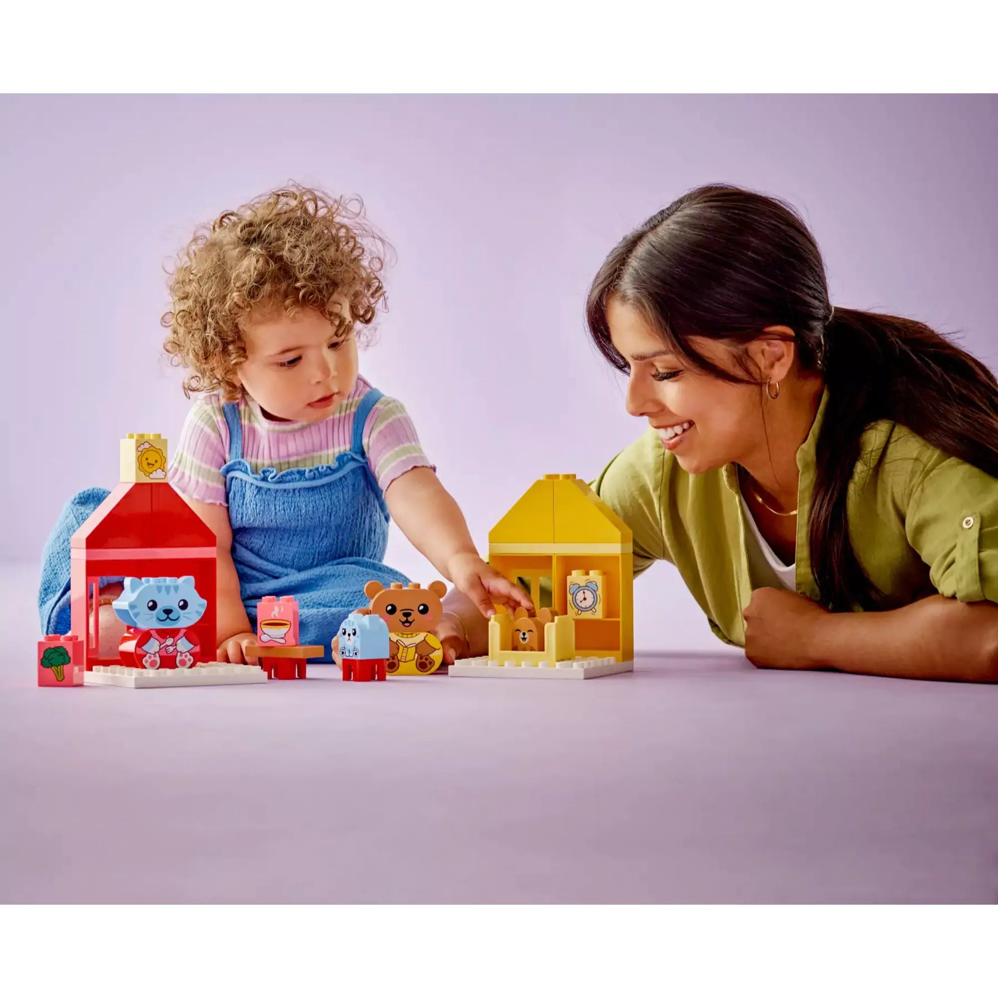 Kislány és anya közösen játszanak LEGO Duplo készlettel – Egy mosolygó anyuka és kisgyermeke közösen játszanak a LEGO Duplo 10414 készlettel, a házikók és figurák köré rendezve.