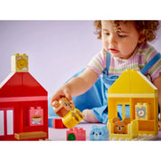 Kislány játszik LEGO Duplo figurákkal – Egy kislány közelről játszik a LEGO Duplo 10414 medvefigurájával a piros és sárga házikók között.