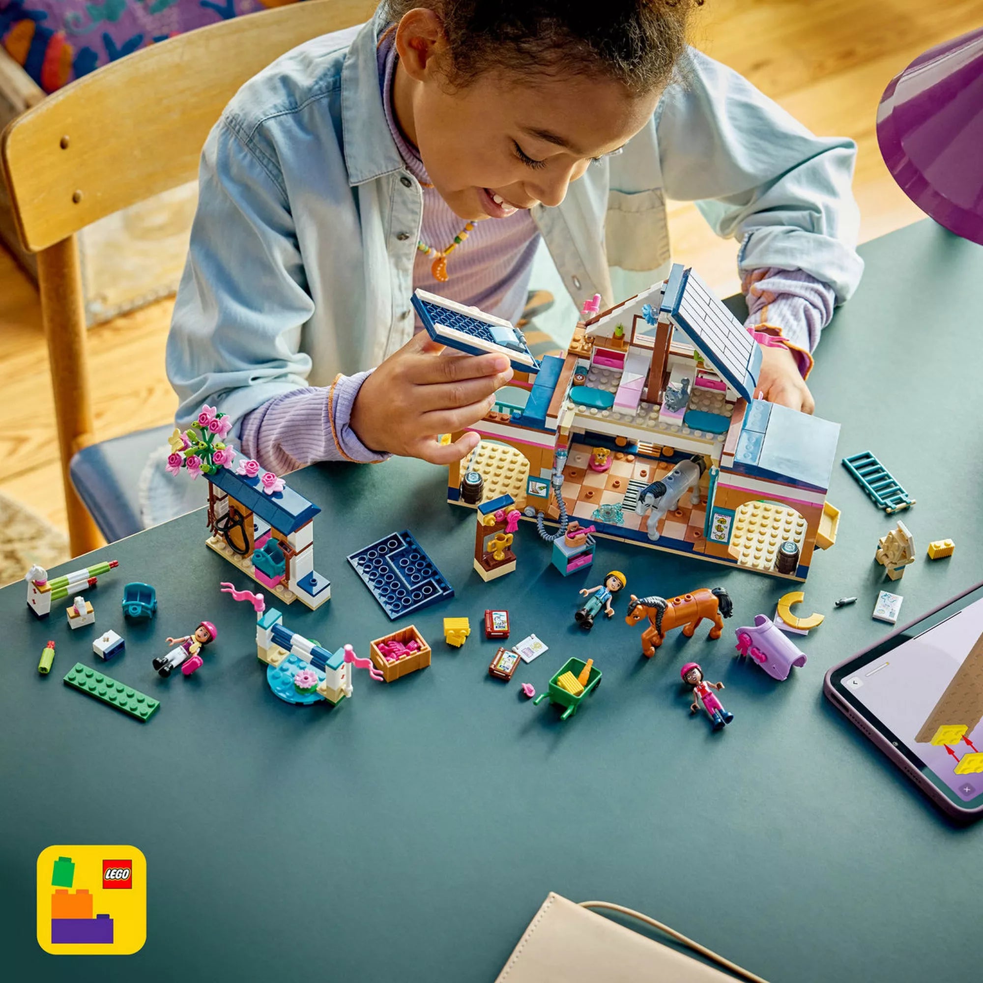 Gyermek LEGO Friends Lovasistálló és lovasakadémia készlettel játszik, az istálló építése közben, lovakkal, minibabafigurákkal és lóápolási kiegészítőkkel.