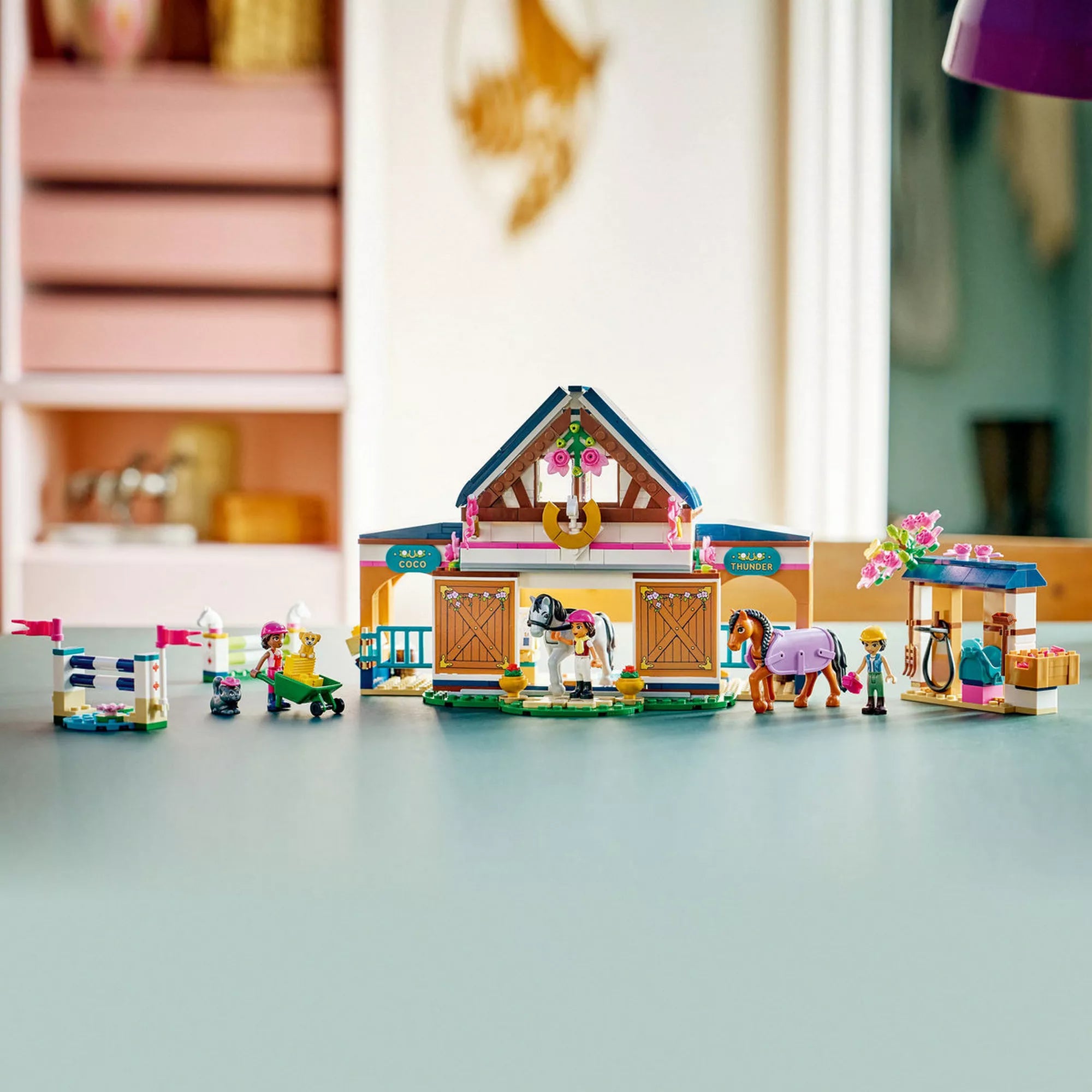 LEGO Friends Lovasistálló és lovasakadémia teljes egészében felépítve, istállóval, kifutóval, ugrató akadályokkal, lovakkal és figurákkal egy asztalon.