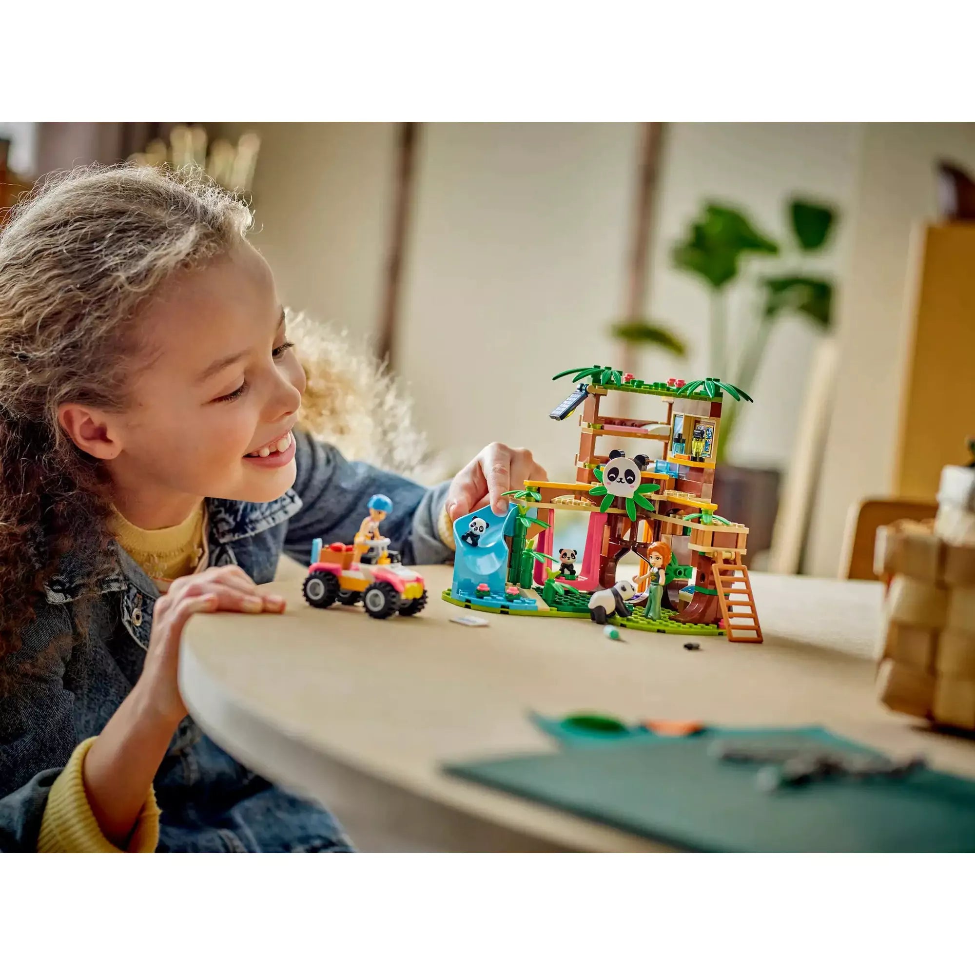 Egy kislány játszik a LEGO Friends Panda Menedékhely (42648) készlettel asztalon, a faépület, csúszda és pandák életre kelnek a játék során.