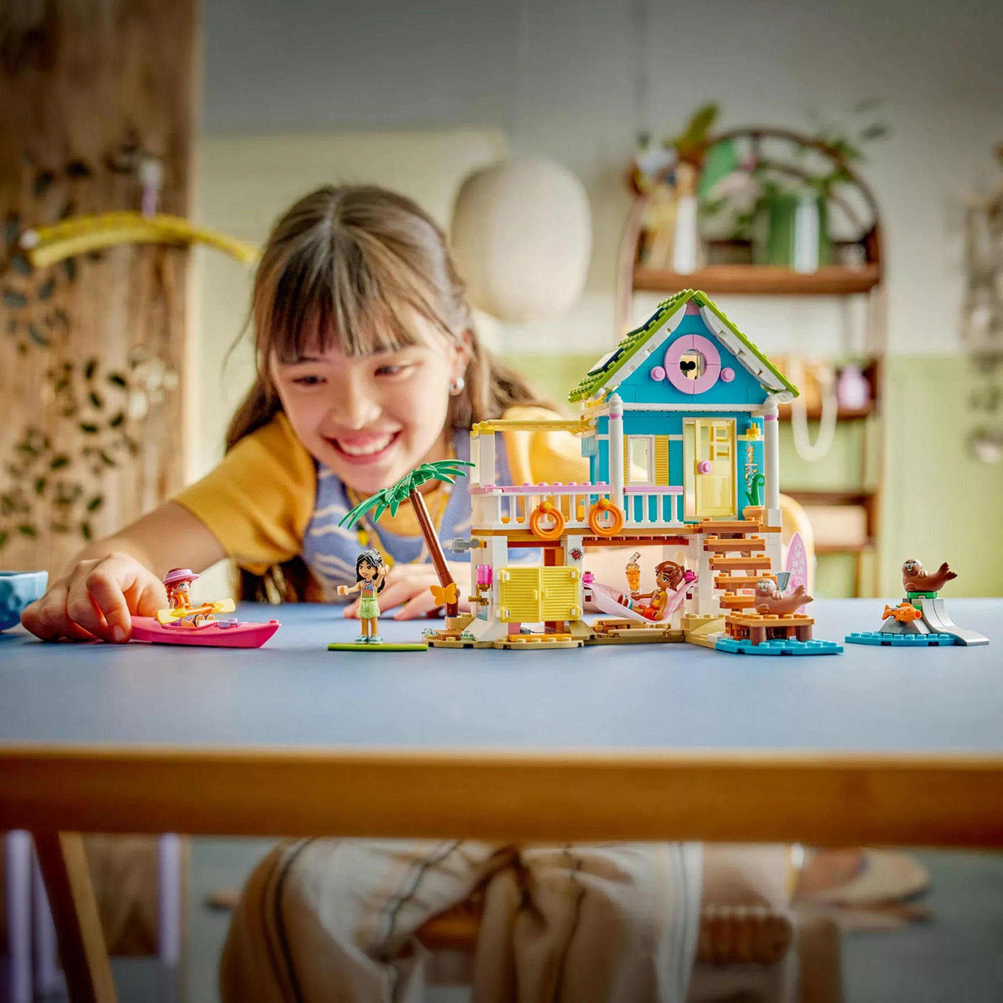 Gyermek LEGO Friends Fókás tengerparti ház (42699) készlettel játszik, a megépített házzal, minibaba figurákkal és fókákkal egy asztalon