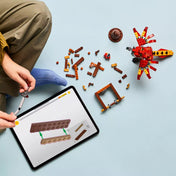 Egy gyermek építi a készletet tableten megjelenített digitális útmutató segítségével, körülötte szétszórt LEGO elemek, köztük a Fawkes figura és a barna állvány részei.
