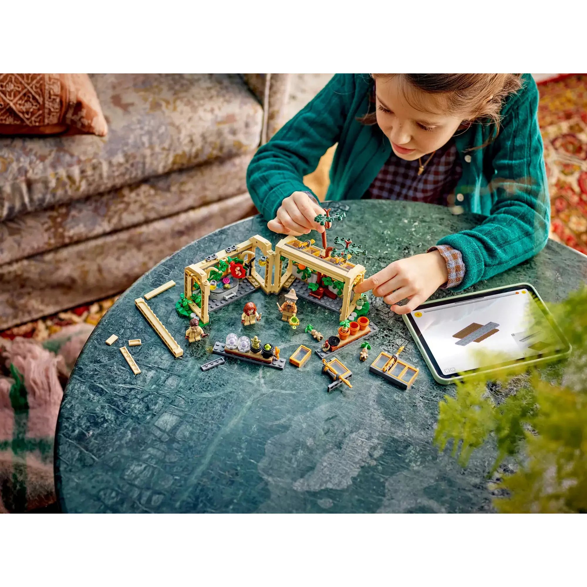 Kislány LEGO Harry Potter Roxfort kastély: Gyógynövénytanóra 76445 készletet épít egy asztalon, mellette egy tablet látható.