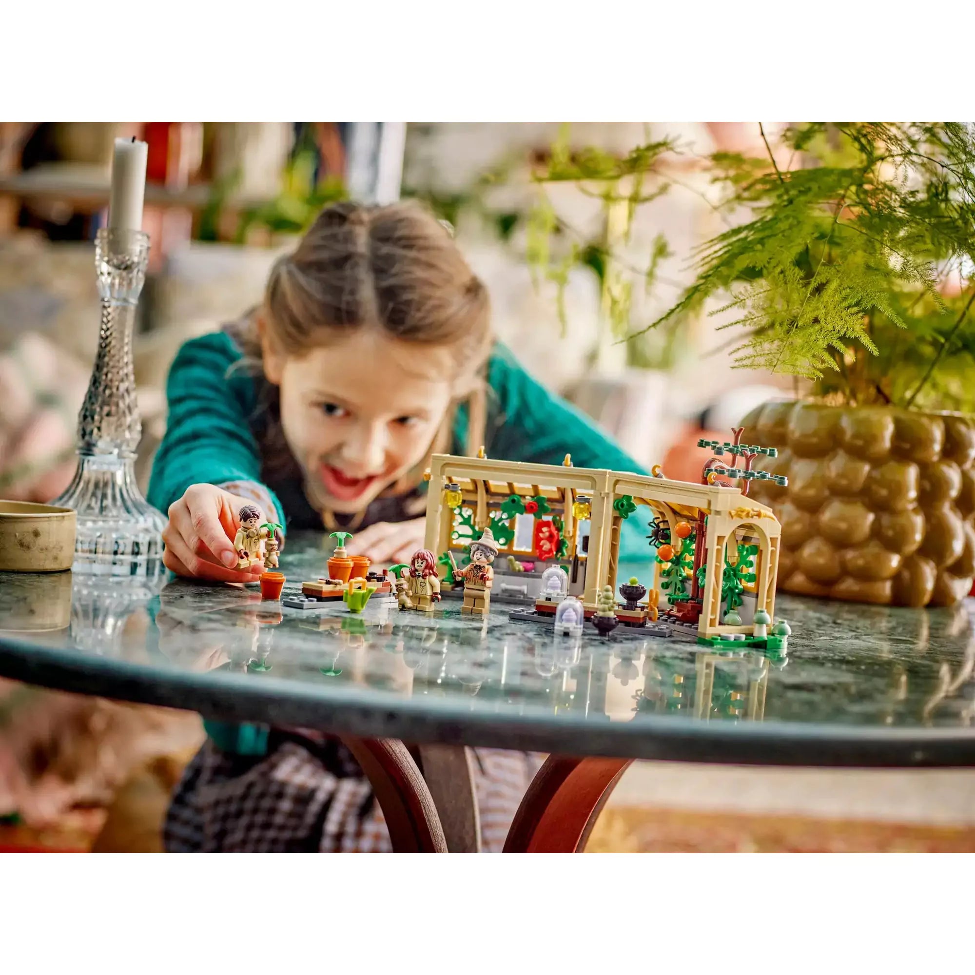 Kislány játszik a LEGO Harry Potter Roxfort kastély: Gyógynövénytanóra 76445 készlettel, karakterek és üvegház elrendezve az asztalon.