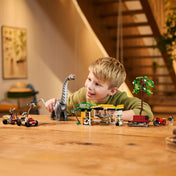 „Egy gyermek a LEGO Velociraptor és Titanosaurus üldözése készlettel játszik az asztalon: a mozgatható Titanosaurus, a tábori állomás, a járművek és a minifigurák mind jól láthatók.”