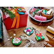 LEGO karácsonyi díszek egy ünnepi asztalon, mellette ajándékcsomagolás és szalagok. A képen a Mikulás, hóember, ajándék és karácsonyfa motívumú LEGO dekorációk láthatók.