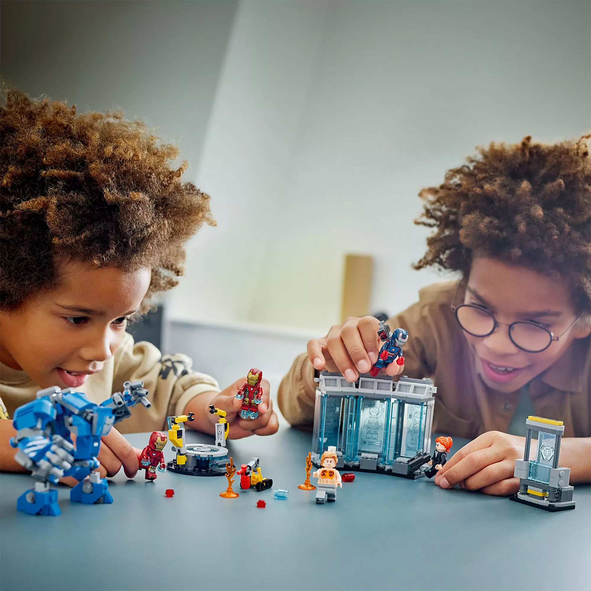 Két gyerek játszik a LEGO Marvel A Vasember laboratóriuma: páncélcsarnok készlettel egy asztalon.