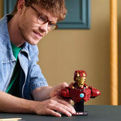 Egy fiatal férfi mutatja a kész LEGO Marvel Iron Man MK4 mellszobrot az asztalon, miközben mosolyogva nézi az összeállított modellt.