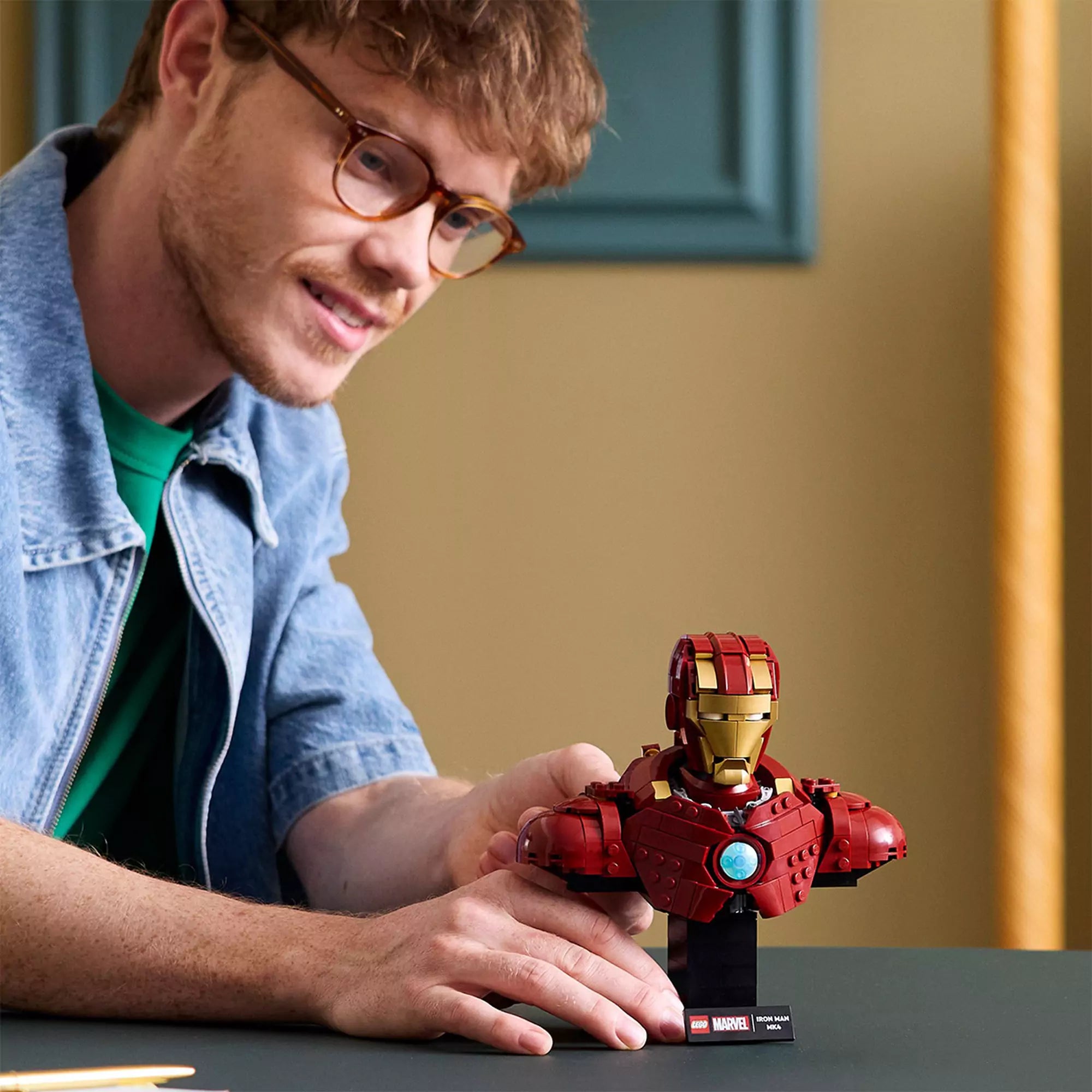Egy fiatal férfi mutatja a kész LEGO Marvel Iron Man MK4 mellszobrot az asztalon, miközben mosolyogva nézi az összeállított modellt.
