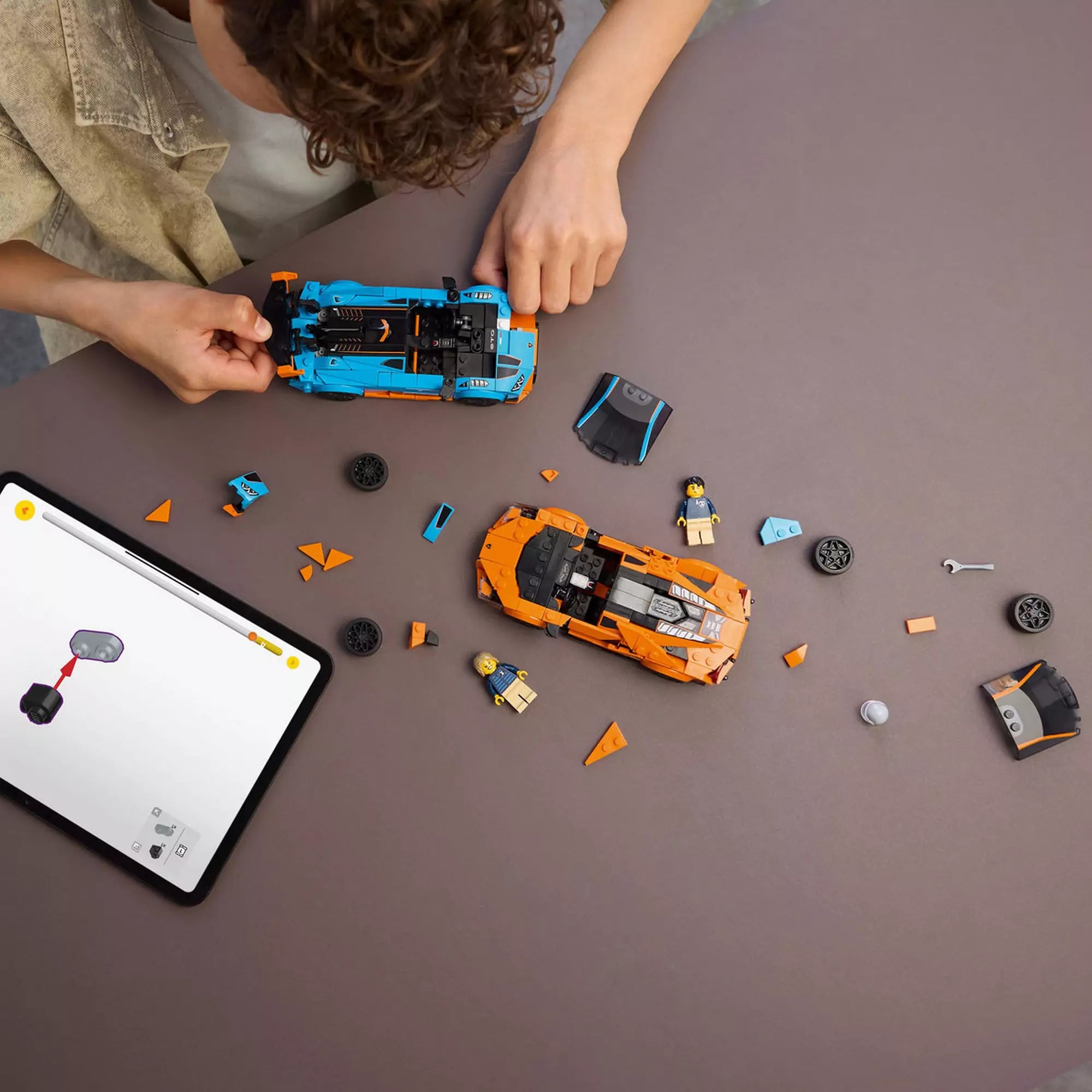 A LEGO Speed Champions 77238 készlet építése közben, szétszedett Lamborghini modellek és minifigurák az asztalon, tableten digitális útmutatóval.
