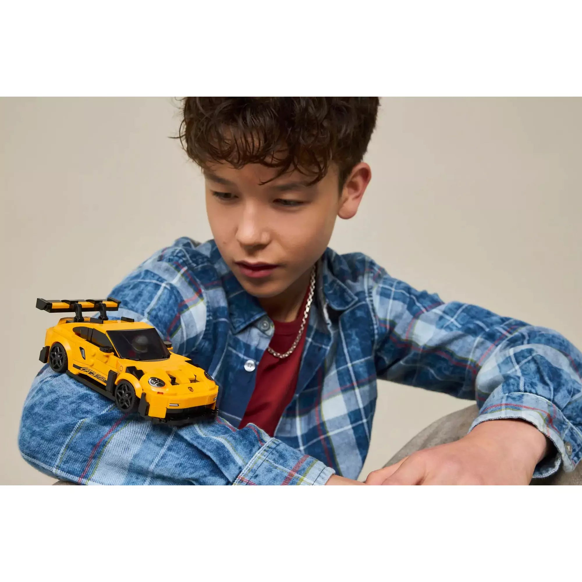  Gyerek játszik a LEGO Porsche 911 GT3 RS (77239) autóval, amely a karján pihen, kiemelve a játék méretét.