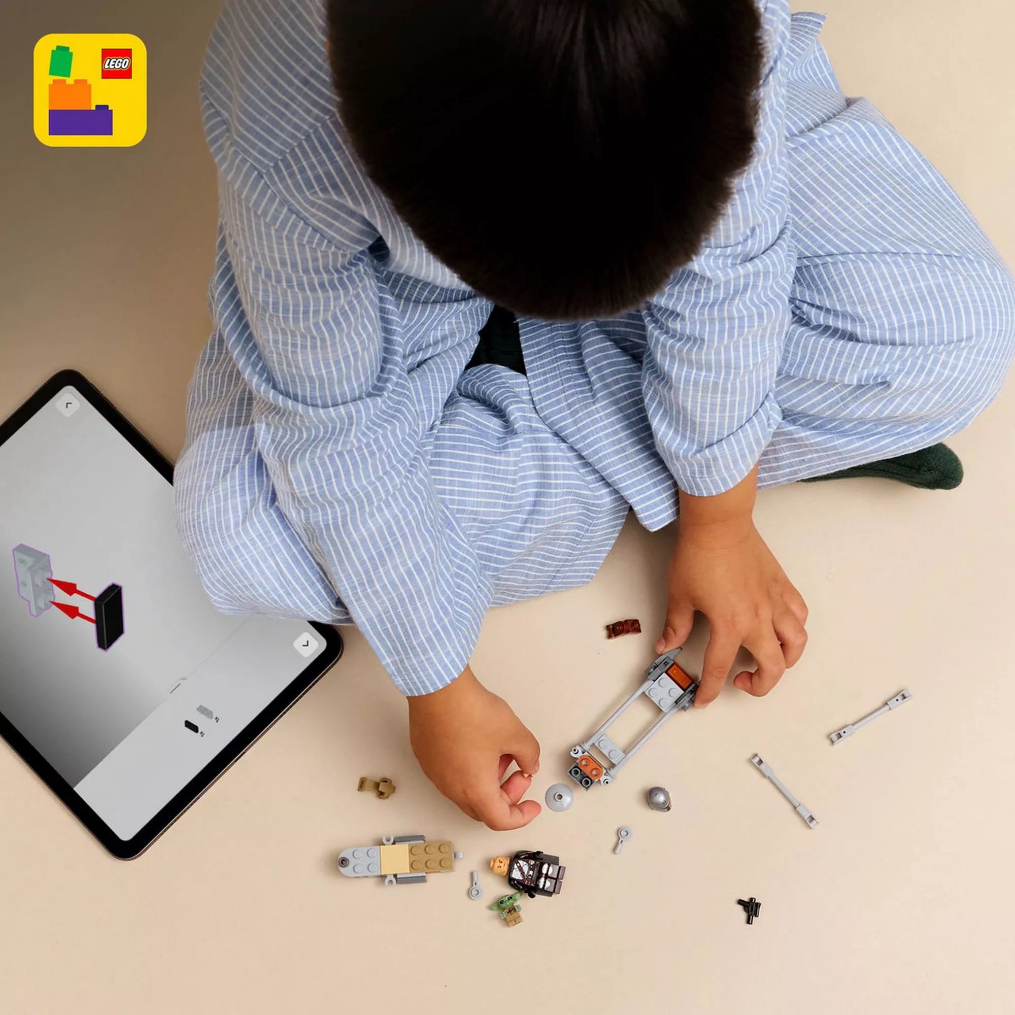 Felülnézeti kép gyermekről, aki a LEGO Star Wars The Mandalorian & Grogu gyorsmotor elemeit építi, mellette a LEGO Builder alkalmazás digitális útmutatója tableten.