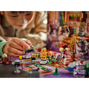 Gyerek kezében egy LEGO droidfigura, előtérben C-3PO, Jawa és különféle ünnepi miniépítmények a LEGO Star Wars Adventi naptár 2025 készletből.