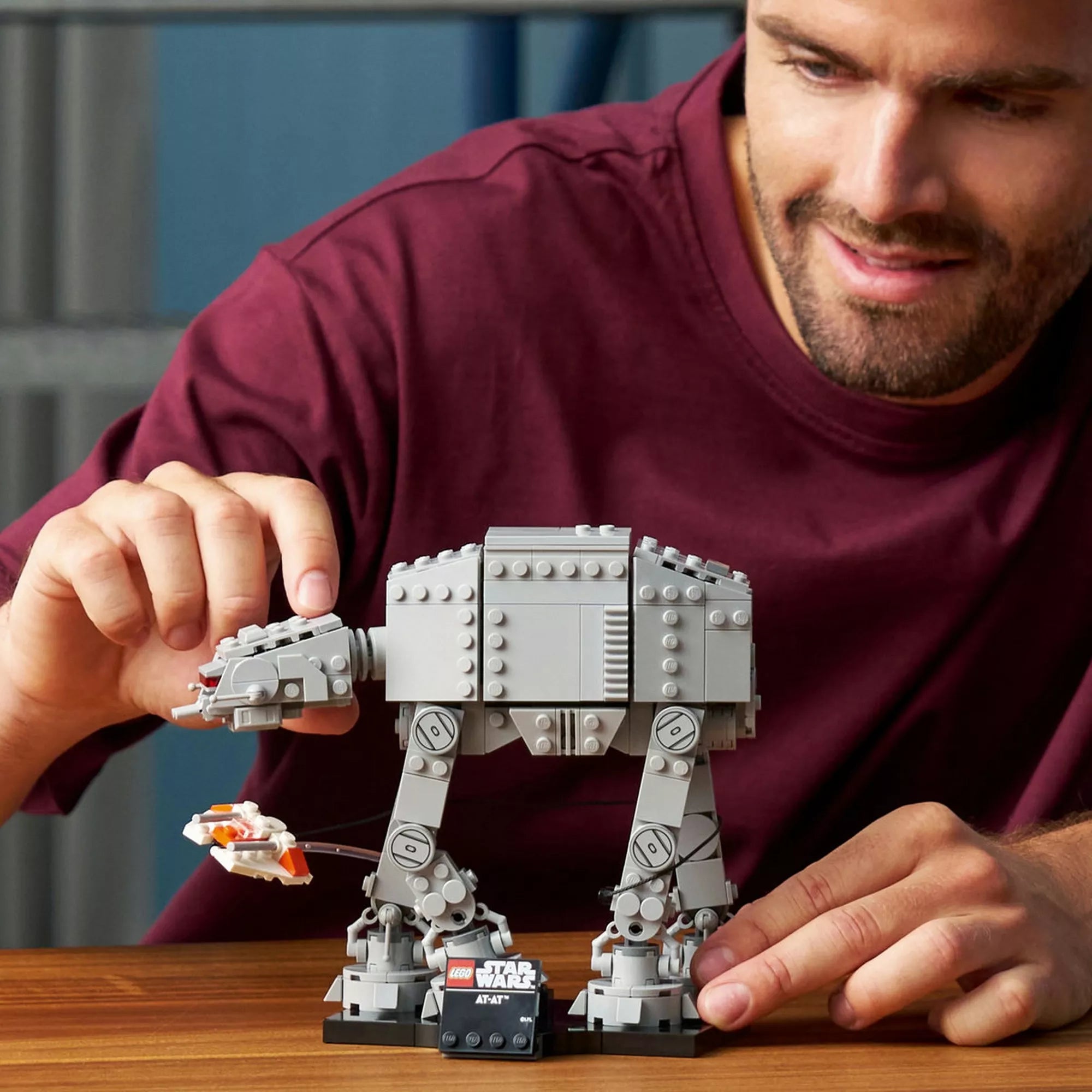 Felnőtt építő játszik és állítja be a LEGO Star Wars AT-AT modellt egy asztalon, a snowspeederrel és a kiállító talapzattal, gyűjtői építési élmény bemutatása.