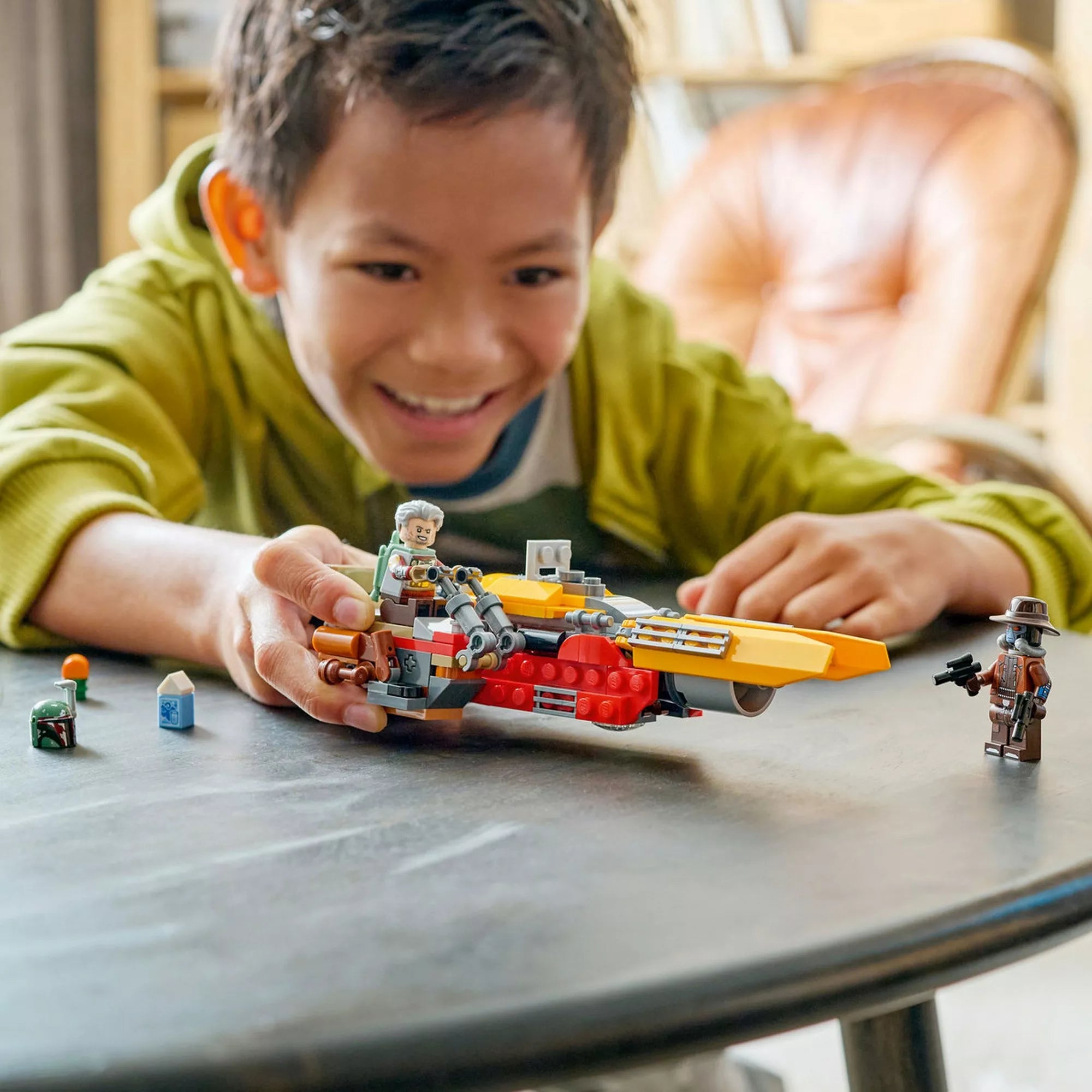 Gyerek játszik a LEGO Star Wars Cobb Vanth speederrel egy asztalon, a készlet minifiguráival és kiegészítőivel, kreatív szerepjáték Star Wars rajongóknak.