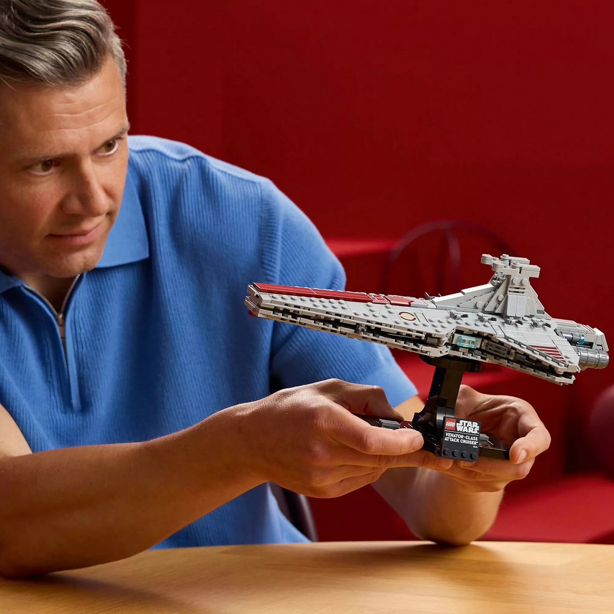 Felnőtt építő tartja kezében a LEGO Star Wars Venator-osztályú támadó cirkáló modellt, a kiállító talapzattal együtt, gyűjtői építési élmény bemutatása.