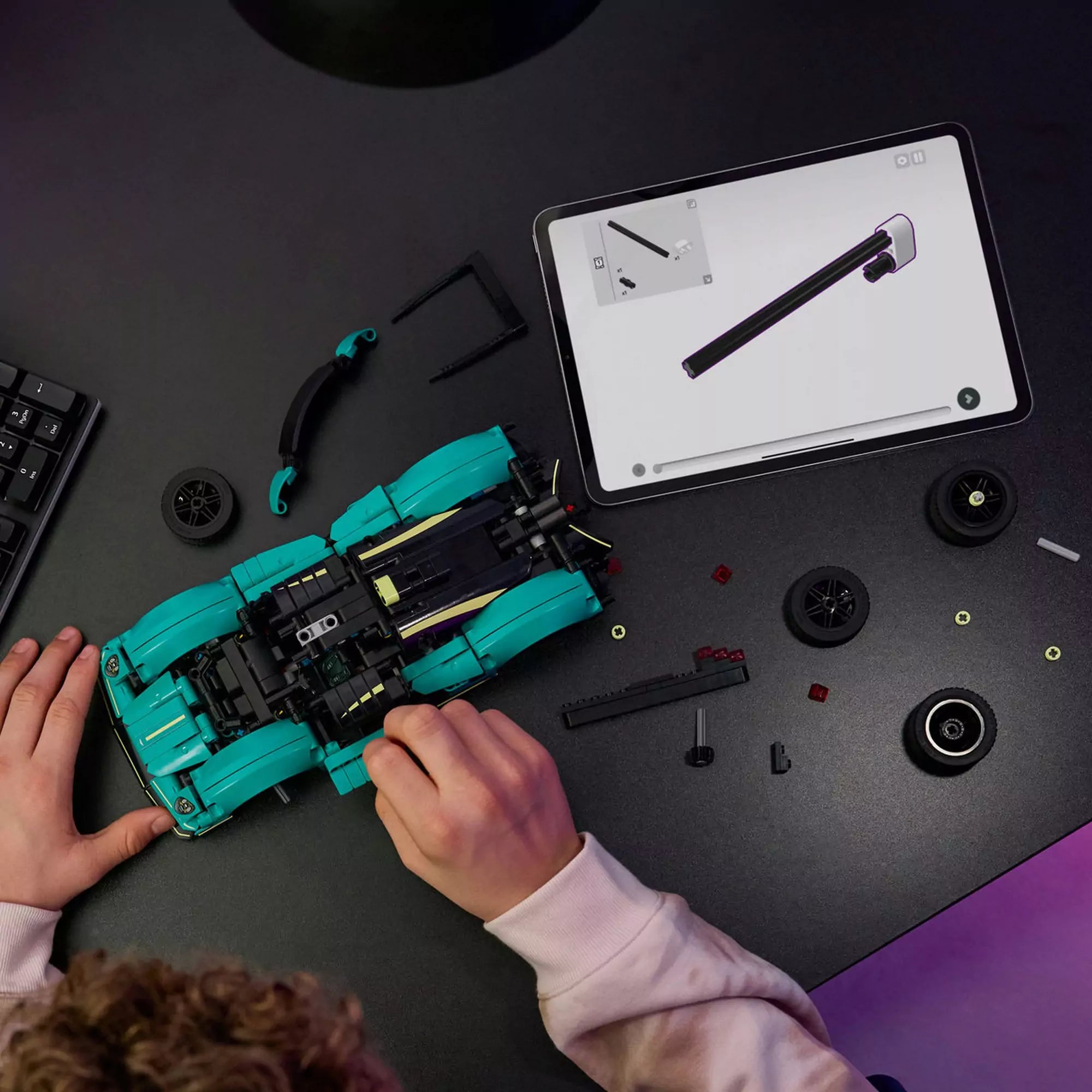  A LEGO Technic Aston Martin Valkyrie (42208) építése közben egy fiú digitális útmutatót követ egy táblagépen, miközben az asztalon több autóalkatrész hever.