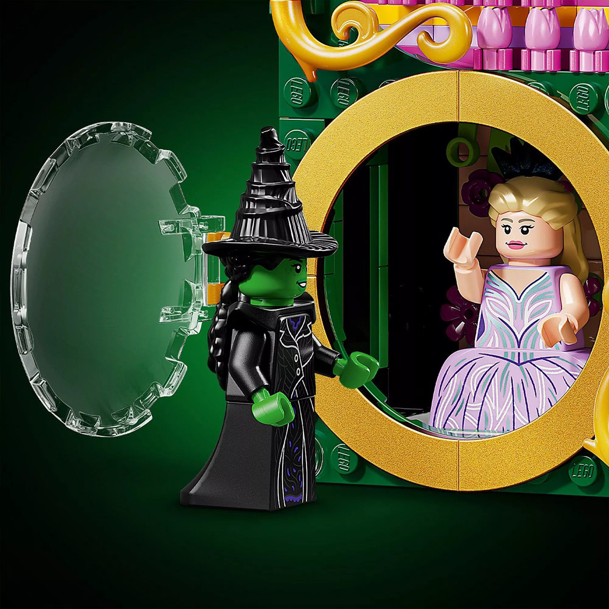 Közeli LEGO jelenet Glinda arany keretes körablakánál, amely kinyitható. Elphaba zöld bőrű minifigurája a nyitott ablak előtt áll, míg Glinda belül ül a díszes rózsaszín háttér előtt. A jelenet a film ikonikus kontrasztját idézi meg.