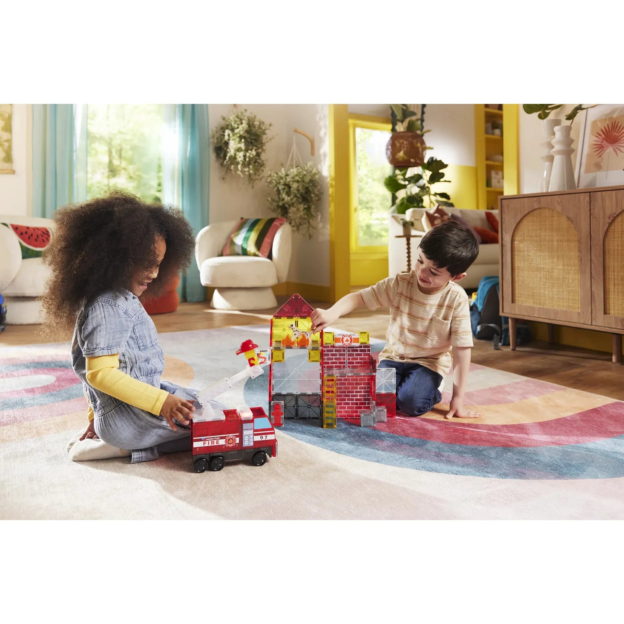 Két gyerek együtt játszik a Magna-Tiles Fire Station készlettel, tűzoltóautóval és lángoló épülettel a nappaliban.