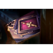 Mysterium társasjáték illusztráció: bársonybetétes fadobozban fekvő arany díszítésű tőr, mellette sakktáblaszerű doboz és szórt játékkorongok misztikus környezetben.