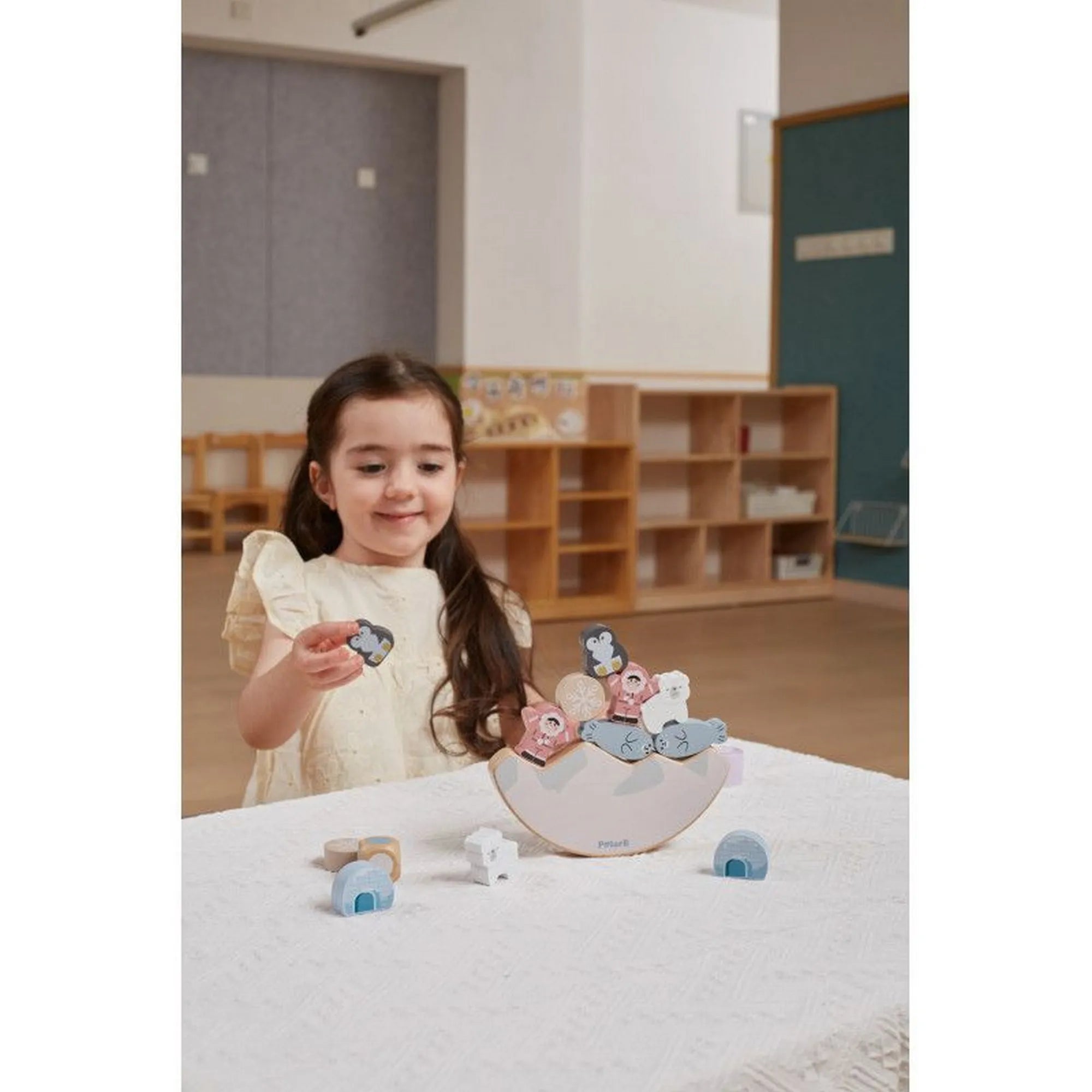 Kislány a Sarkvidék témájú fa állatos egyensúlyozó, PolarB, Viga figuráit helyezi a billegő alapra.