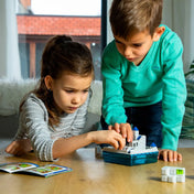 Két gyerek az asztalnál együtt rakja ki a lépcsős logikai pályát, a feladványfüzet mellett.