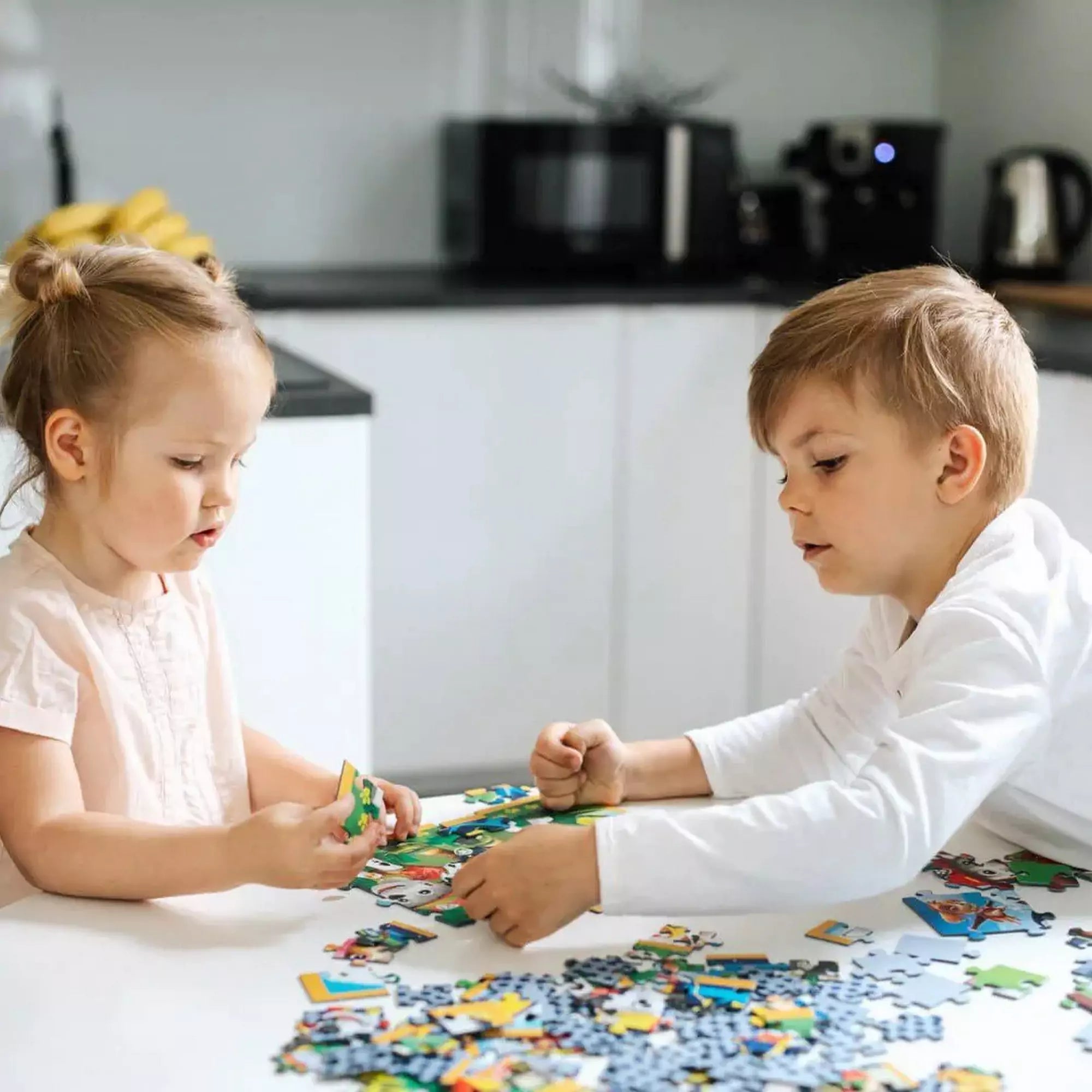 Egy kisfiú és egy kislány egy asztalnál puzzle-t raknak ki, élvezve a játék örömét.
